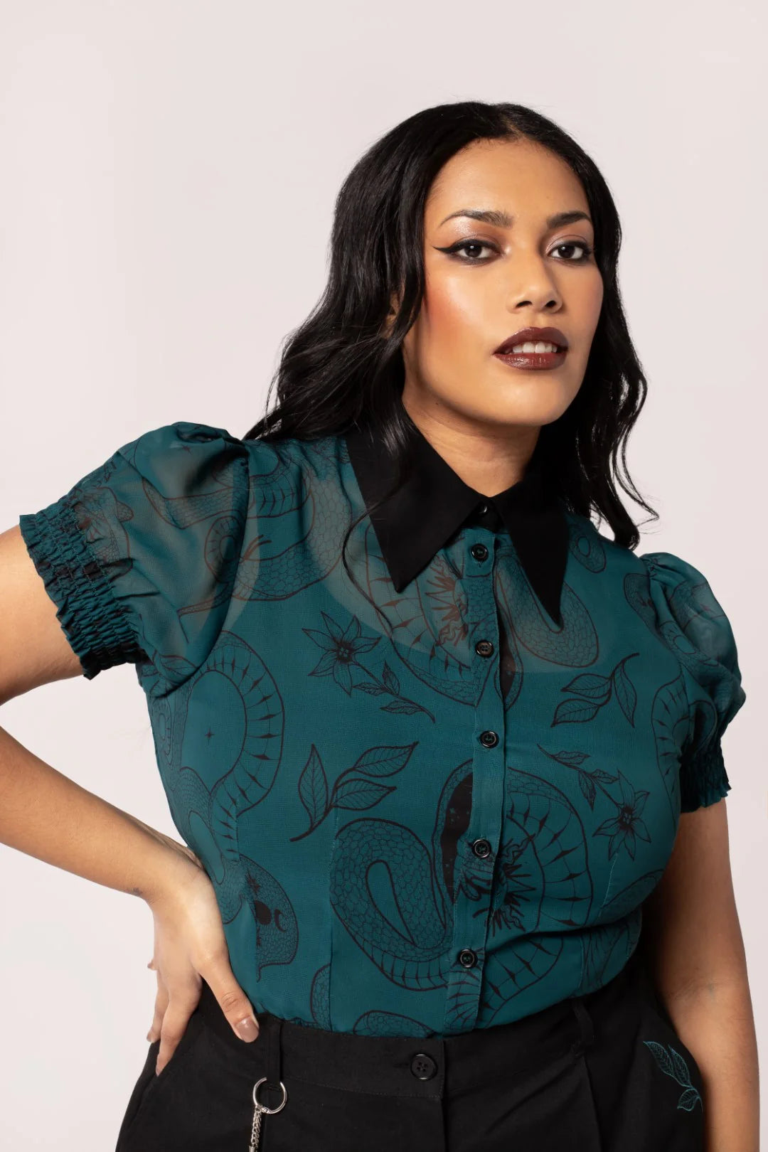 Woman wearing a teal blouse with black collar and embroidery on a white background